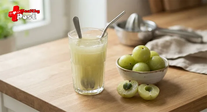 Glass of pale green amla juice next to whole and halved Indian gooseberries on a wooden counter